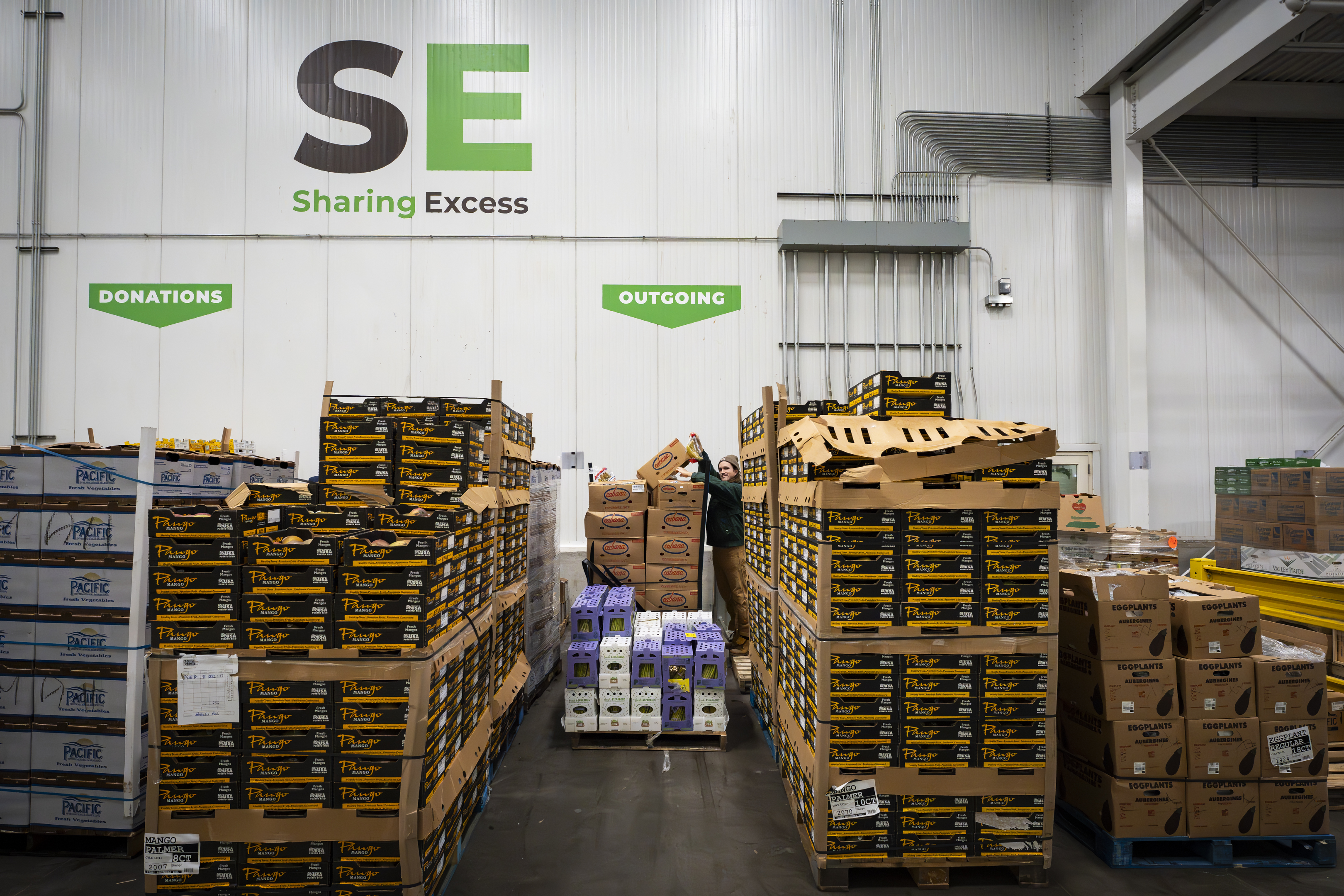 Sharing Excess warehouse with stacked produce and SE logo on the wall